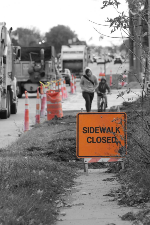 Two pedestrians walk on a sidewalk that was closed by a construction site.  