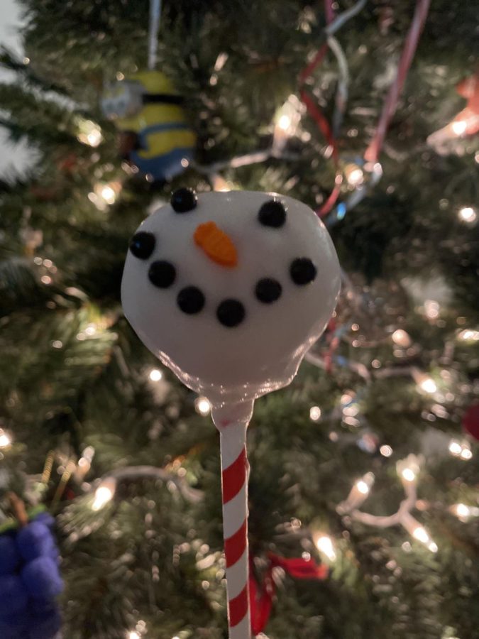 Photograph of a delicious homemade  snowman cake pop with a Christmas tree in the background.
